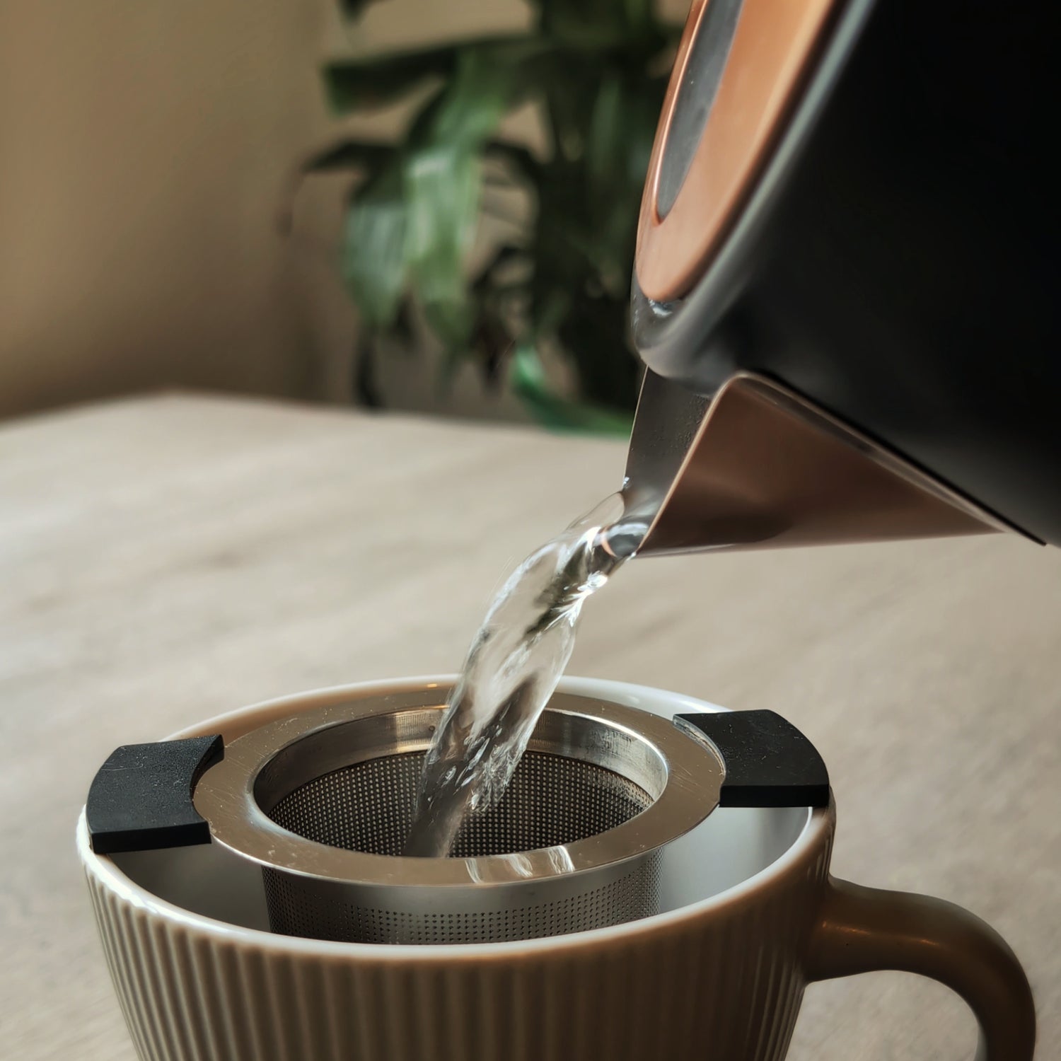 Tea pot pouring water into a teacup with a blurred plant in the background